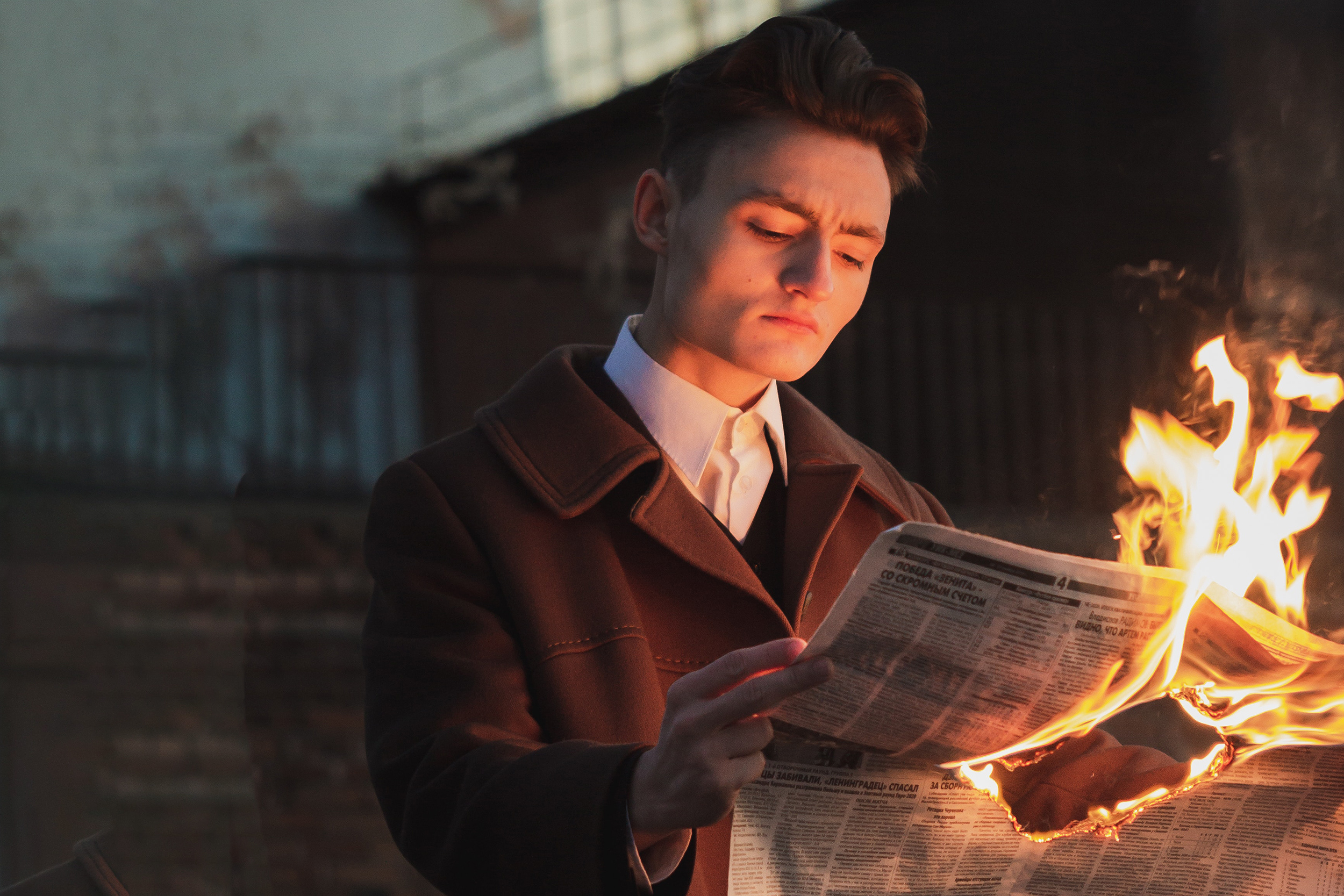man in brown jacket calmly reading burning newspaper