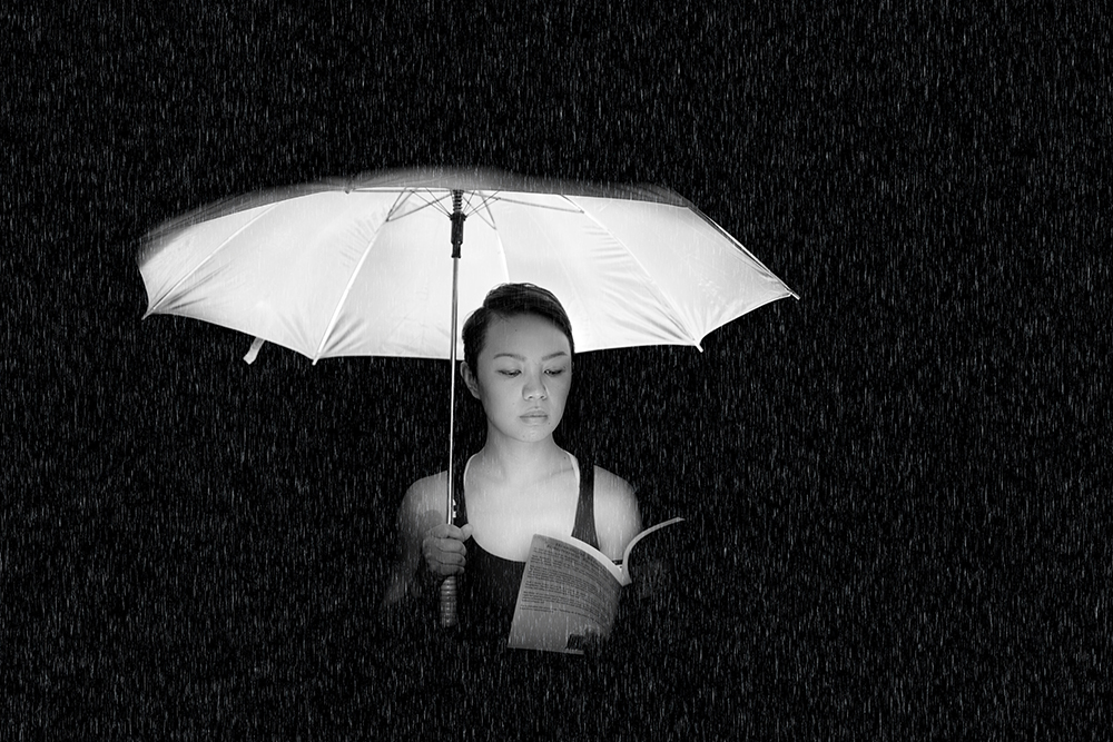 Black and white image of woman holding umbrella lit from below with a book