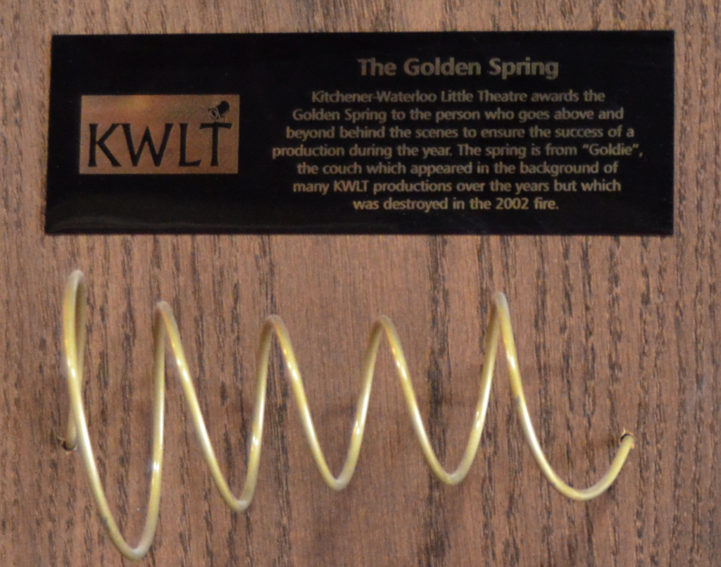 The Golden Spring Award, consisting of a sofa spring that has been bronzed and affixed to a wooden plaque. The caption explains that the spring is from a sofa called "Goldie" that sat in the lobby of the theatre and was destroyed in the fire of 2002.