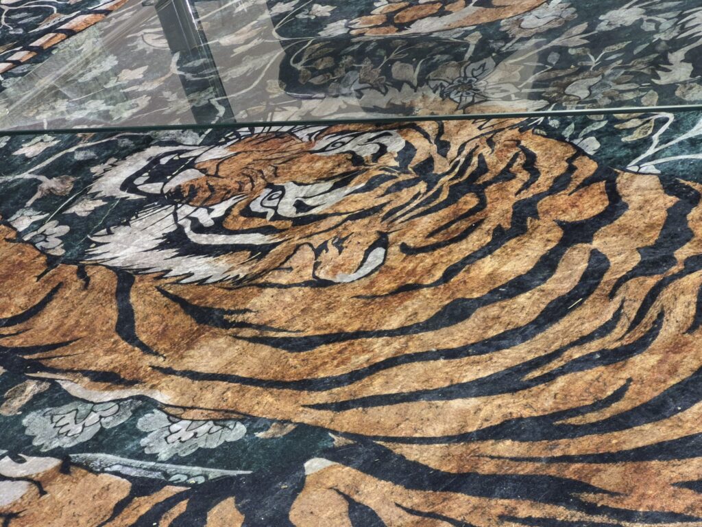 A carpet showing a stalking tiger, visible underneath a glass-top coffee table